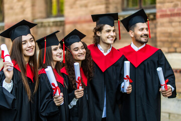 Successful excited five graduates in robes standing in row and showing certificate.