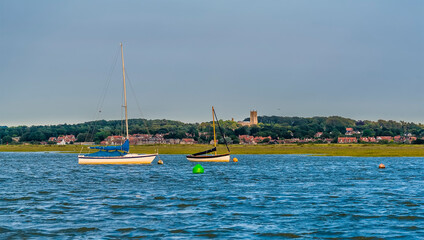 Fototapeta na wymiar Sailing boats moored in the estuary of the River Glaven, Norfolk with the village of Blakeney in the distance