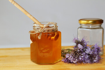A glass jar of honey and an empty jar stand on a wooden table. Wooden spoon bee honey in a glass container with med. Flowers of phacelia. Blue flowers. At close range.
