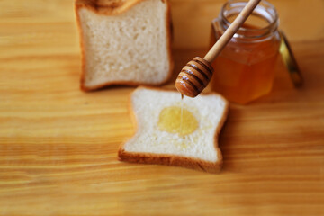 Bread product with honey. With a wooden stick for honey, we grease a piece of bread. A glass jar of med stands on a wooden table. Preparing a snack. Sweet food. Close-up and top view.