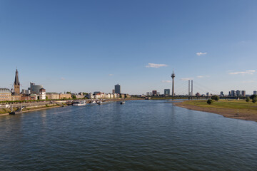 Fototapeta na wymiar Outdoor panoramic sunny scenic cityscape view of Düsseldorf city, Germany, with promenade walkway on waterfront through old town and downtown, view from the bridge over Rhine River. 