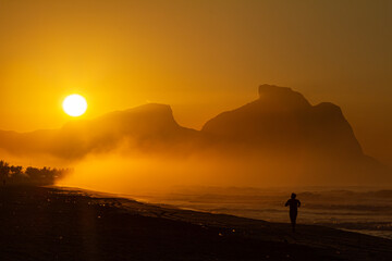 silhueta de um homem exercitando-se na praia ao nascer do sol, com a bela pedra da Gávea em segundo plano