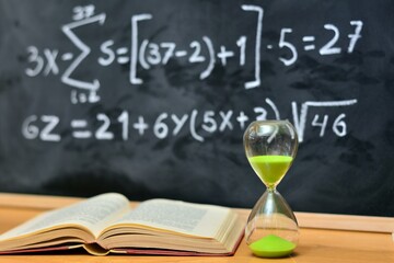 Reloj de arena y libro sobre la mesa, con fondo de pizarra desenfocada