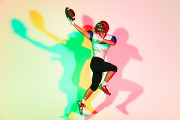 Fototapeta na wymiar American football player isolated on gradient studio background in neon light with shadows. Professional sportsman during game playing in action and motion. Concept of sport, movement, achievements.