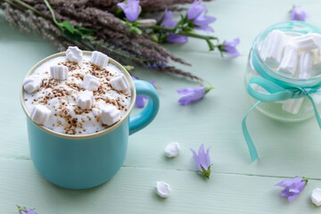 Delicious mocha with white marshmallows on an azure background with lilac flowers.