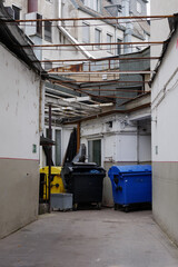 View of narrow street between building   , service area behind buildings with plastic waste garbage container bin under broken roof.