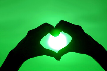 Obraz premium Pop art style silhouette of female's hand posing HEART sign against shiny sun on green colored sky