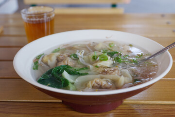 Close up view of hot Chinese Wonton dumping Soup with Pak Choi and cold tea on wooden outdoor table.
