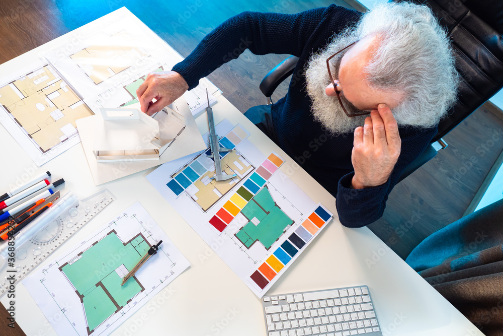 Poster interior designer at work. a gray-haired architect at his desk. the man is filmed from above at a ta
