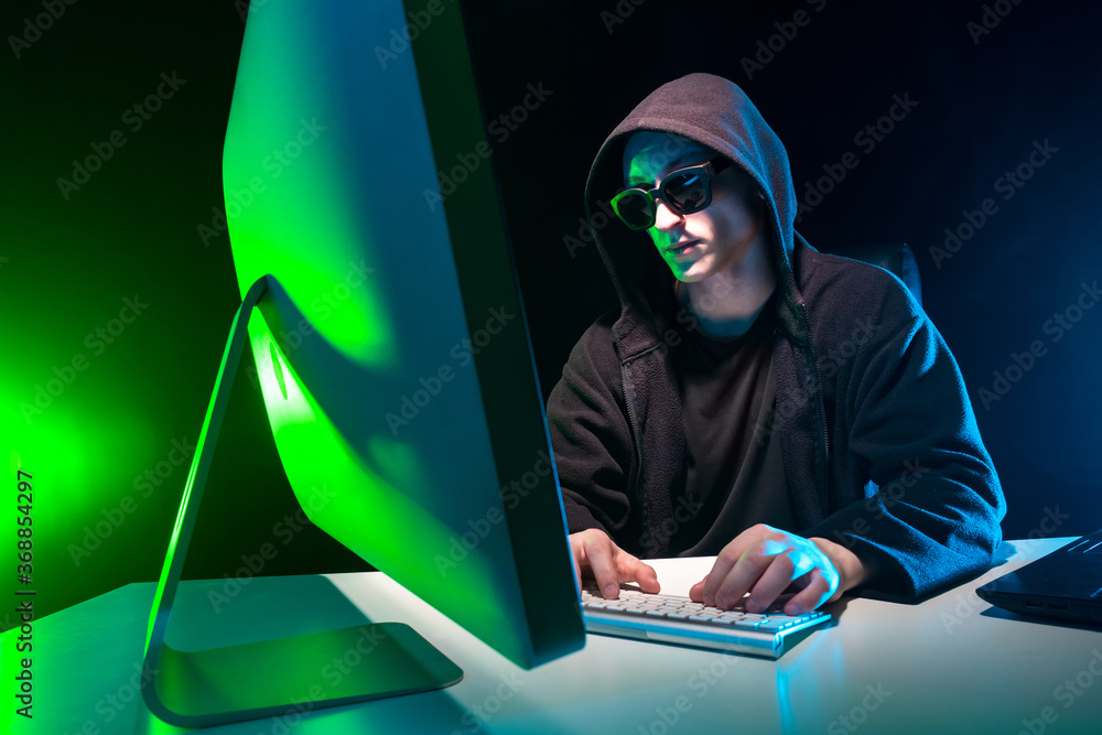 Poster cybercrime. a man hides his face when working at a computer. virtual crimes. hacker in a black hoodi