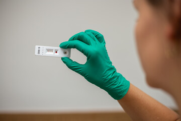 Woman doctor looking at Covid-19 rapid test wearing green latex gloves