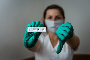 Woman doctor showing positive Covid-19 rapid test wearing green latex gloves