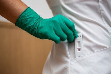 Woman doctor taking out Covid-19 rapid test from a coat in green latex gloves
