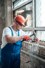 A hardworking builder works on a construction site using a hammer to destroy old brick walls, looking very concentrated