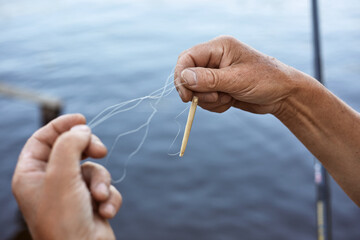 Faceless male untangles knot of fishing line over water on background, unknown person holding...