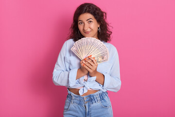 Closeup portrait of young girl holding bunch of money in hands and looking directly at camera, being happy, expressing happiness, celebrating her winning.