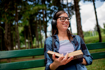 Young woman in the park listening to music and reading book