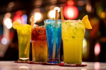 Fresh multicolour alcoholic beverages in a fine dine restaurant garnished with lemon piece and ecofriendly wooden straw with bokeh