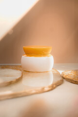 White cosmetic cream jar with orange lid on light pastel color background. Natural minimalism, clean concept. Minimal styling, still life. Beauty blogging, branding layout,  skin care ad mock up