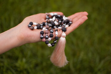 Female hand holding a buddhist japa mala made from 108 natural stones beads for meditation on green...