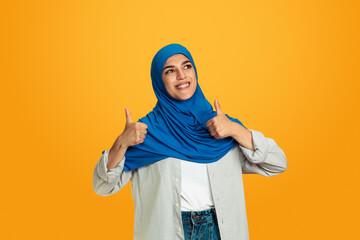 Thumbs up. Young muslim woman isolated on yellow studio background. Stylish, trendy and beautiful female model. Human emotions, facial expression, sales, ad, shopping concept. Copyspace.