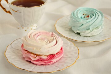 Pink and turquoise meringue cakes with a cup of tea on a white tablecloth close-up.
