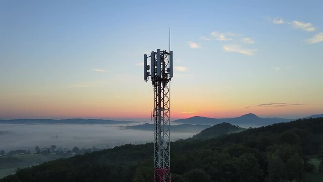 Aerial: 4G & 5G telecommunication tower on remote hilltop at sunset, rising view