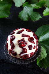 Soft dessert cheese with cranberries and grape leaves on a black background. Sweet cheese for Breakfast. Delicious dessert. Copy of the space. Top view. Vertical photo.