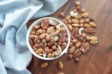 Wooden bowl with mixed nuts on table top view. Healthy food and snack. Walnut, pistachios, almonds, hazelnuts and cashews.