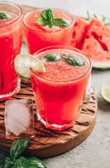 Watermelon lemonade with lime and fresh basil leaves on concrete background. Refreshing summer drink