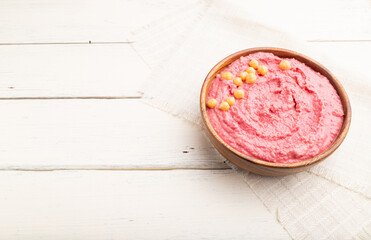 Hummus with beet in wooden bowl on a white wooden background. Side view, copy space.