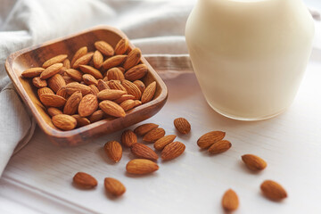 Almond milk in glass with almonds in wooden bowl on a white wooden table