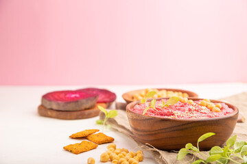 Hummus with beet and microgreen basil sprouts in wooden bowl on a white and pink background. Side view, selective focus, copy space.