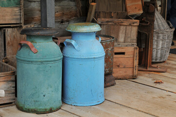 Old metal milk cans on a wooden porch among old wooden boxes