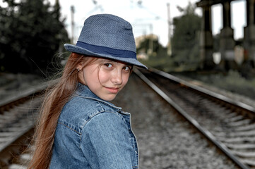 Portrait of a beautiful girl in a blue hat next to railway