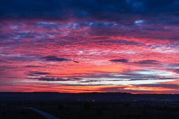 Passenger jet airplane trimmed against the clouds taking off during very red sunrise from spanish airport in a cloudy day