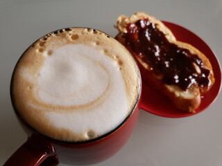 Cup of homemade cappuccino on the table. Sweet bread with jam on the side. Morning coffee time.