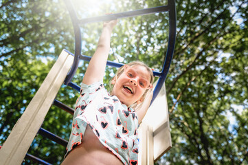 Happy teenage girl playing on the playground. Child girl hanging upside down on the playground. Smiling teenager girl playing at a sports construction
