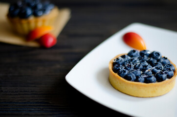 Blueberry tart cake on white plate, decorated with red candies on dark wooden table, close up
