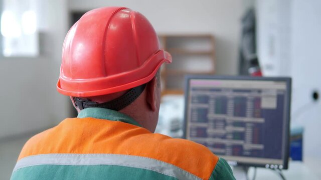 Factory operator in a helmet at work near computer
