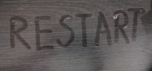 The word restart written with a finger on a dusty blackboard. Business concept.