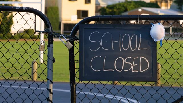 School closed sign with protective face mask hanging on a padlocked gate, school closed or shutdown concept amid coronavirus fears and panic over contagious virus