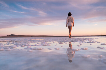 Beautiful woman's back on a sunset background. Reflection of a girl in the water. Salt lake pink sunset.