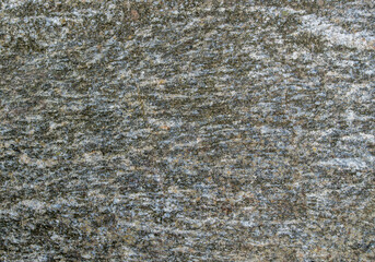 A fragment of the surface of a gray granite stone with greenish and brown spots, stripes, irregularities, grooves and islands that form an abstract pattern. Mineral natural background.