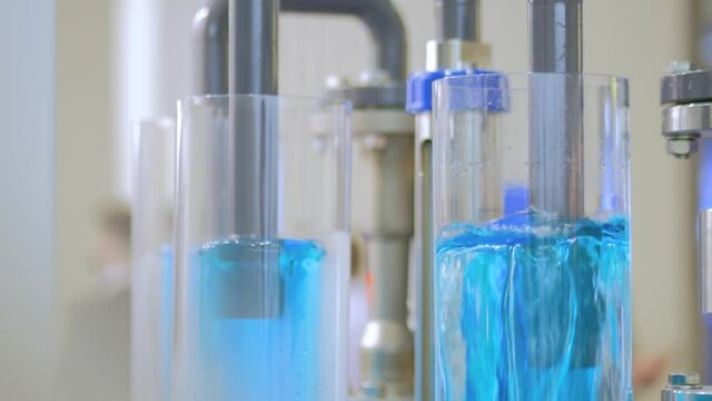 Mass flow meter - moving blue liquid in glass tube at pharmacy factory, medical exhibition: close up. Automated technology, measuring, pharmaceutical, healthcare, laboratory equipment concept