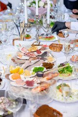 Male hand in black glove picking delicacy with a fork from a seafood and sashimi feast elegant table setting