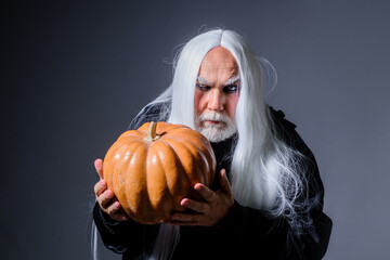 Devil vampire man with orange pumpkin. Handsome Demon with Jack o lantern. Happy Halloween. Evil...