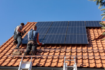 Workers installing solar electric panels on a house roof in  Ochojno. Poland