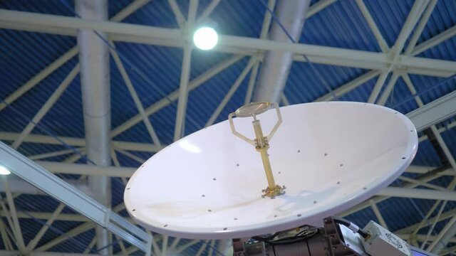 White rotating satellite dish antenna, VSAT parabolic receiver using to receive or transmit information at telecommunication exhibition - slow motion, low angle. Broadcasting, technology concept