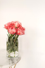 Beautiful pink peony flowers bouquet in glass vase on marble table on white background